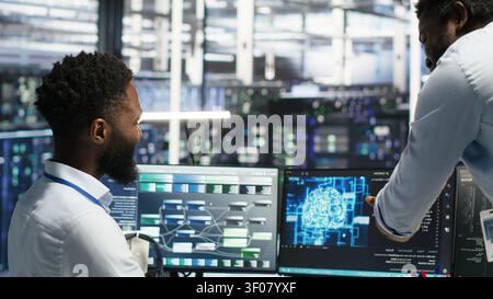 Satisfied server facility supervisor praising technical work from systems engineer working with neural network models to set up hardware. Stock Photo