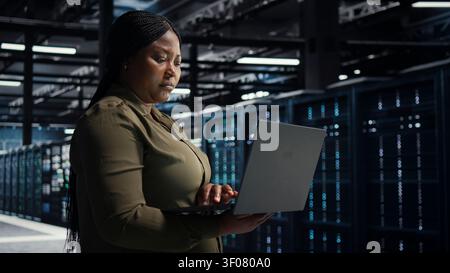 Software engineer in server facility working with notebook computer to update systems for increased stability. Stock Photo