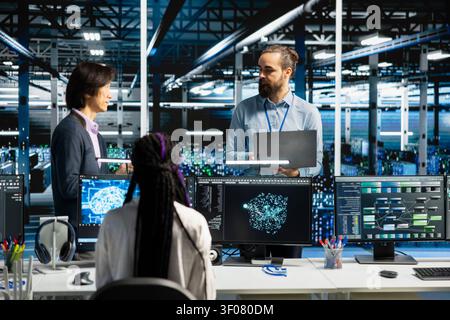 Engineers brainstorming in high tech high tech server room, refining AI model parameters to upgrade systems, while scheduling deep learning checkup for equipment supercomputers server hardware. Stock Photo