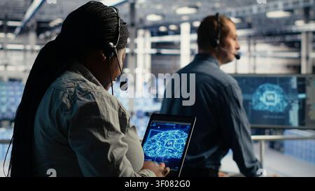 Data center technical support staff member working with AI on a digital tablet to guide customers. Technical specialist in server facility helps users fix system errors on servers applying AI. Stock Photo