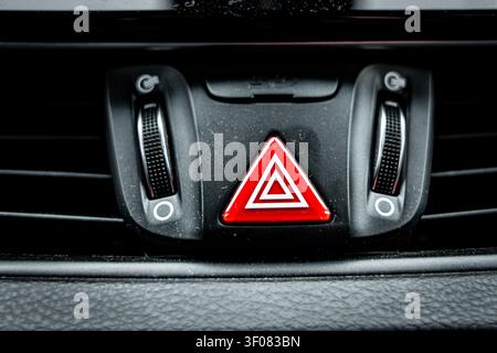 A detailed view of a car's dashboard, focusing on the red triangle warning light and surrounding vents. Stock Photo