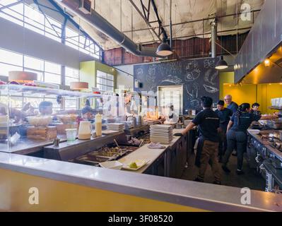 Washington state, United States, JUN 21, 2026 - Chefs and kitchen staff work behind a stainless steel counter in a busy restaurant with a chalkboard m Stock Photo