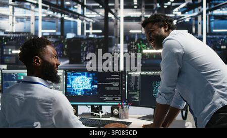 Satisfied server facility supervisor praising technical work from systems engineer working with neural network models to set up hardware. Stock Photo