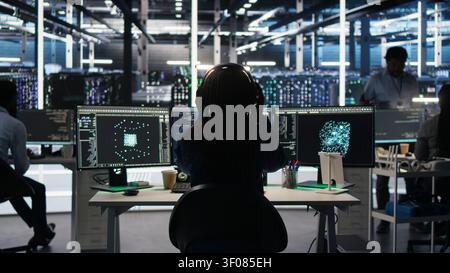 Data infrastructure center technical specialist working with algorithms to assess large datasets, wearing headphones, while IT professional working with AI to recognize data patterns listening music. Stock Photo