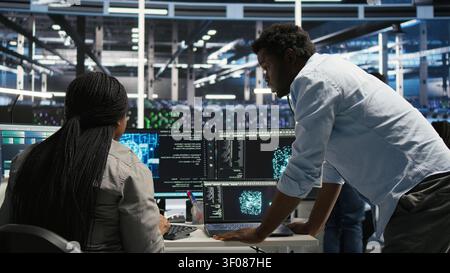 Server facility engineering team works with AI ML models to set up equipment. Teamworking colleagues work on AI programming tools in server environment, optimizing system. Stock Photo