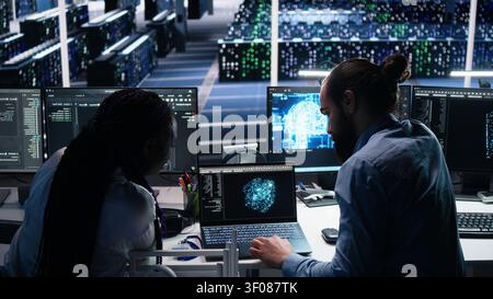 Server facility admin teaching trainee to check AI network working with AI. IT expert and African American woman at work applying AI to supervise servers powering ML. Stock Photo