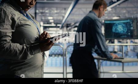 Software development team uses a tablet in a server room to review test results and confirm reliable system operation. Stock Photo
