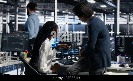 Lead engineer and trainee use a PC in a server room to develop neural network software and implement machine learning technology. Stock Photo