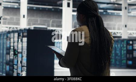 Woman walking through server facility rows of servers, rolling out advanced cooling and power management solutions. IT expert supervising server environment, reducing energy consumption. Stock Photo