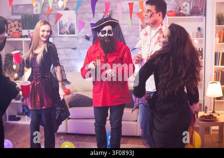 Cheerful young woman dressed as a vampire with bloody lips celebrates Halloween with funny friends in a party atmosphere with theatrical styling, dark atmosphere and clear costume character detail. Stock Photo