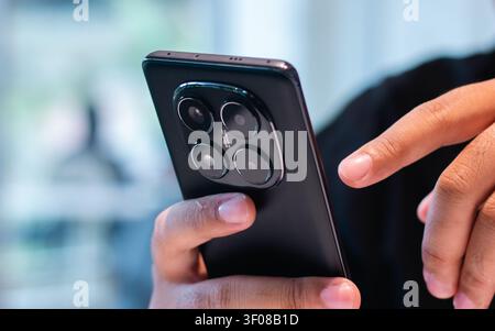 A close up view of a person's hand holding a modern smartphone against a dark background with soft focus, showcasing the sleek design and multiple cam Stock Photo