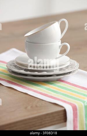 Stacked white teacups and plates on striped cloth Stock Photo