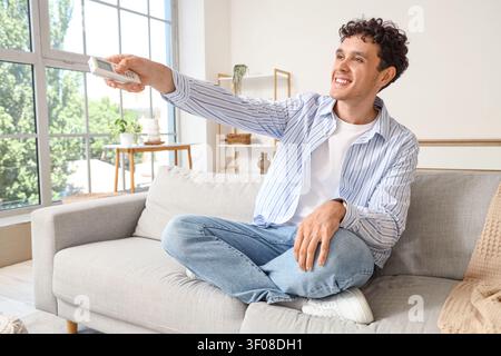Young man using remote control on sofa in living room Stock Photo