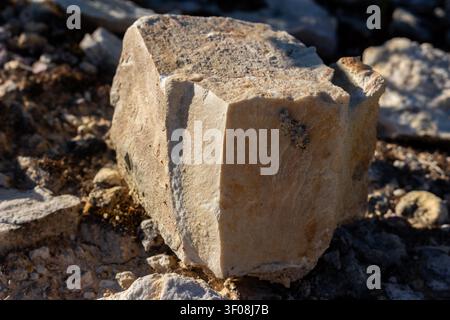 Large piece of rough marble-like limestone sits in an abandoned quarry, showcasing natural texture, earthy tones, and geological layers under bright s Stock Photo