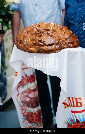 A close-up shot of a beautifully decorated traditional Ukrainian wedding bread, known as korovai, resting on a white embroidered towel (rushnyk). Stock Photo