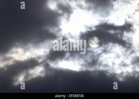 Monotone view of the sun shining through dramatic dark storm clouds Stock Photo