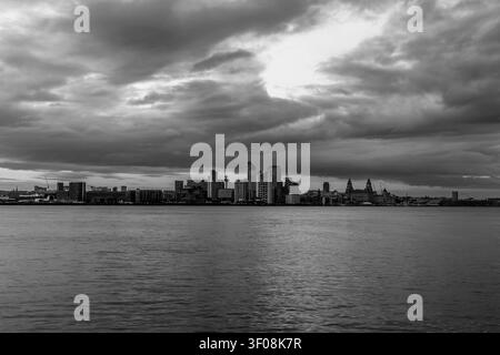 Liverpool skyline stretching along waterfront beneath heavy storm clouds across River Mersey in black and white Stock Photo