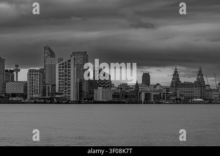 Liverpool skyline stretching along waterfront beneath heavy storm clouds across River Mersey in black and white Stock Photo