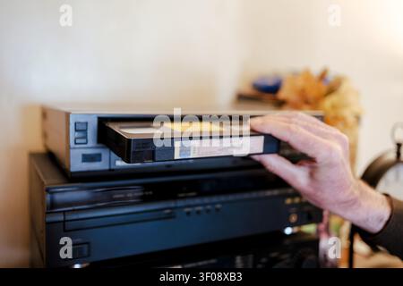 Hand inserting black vhs cassette into a vintage videocassette player, bringing back analog nostalgia Stock Photo