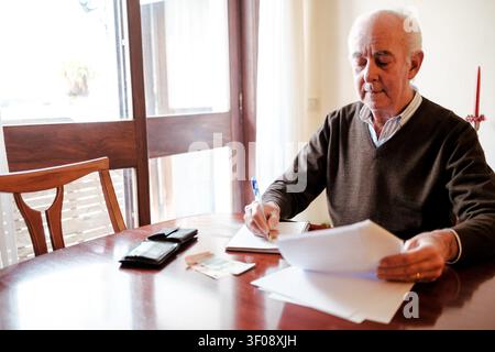 Senior man calculating expenses and making notes on paper at home Stock Photo