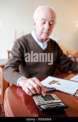 Senior man calculating finances and budget using a calculator and coins on a table Stock Photo