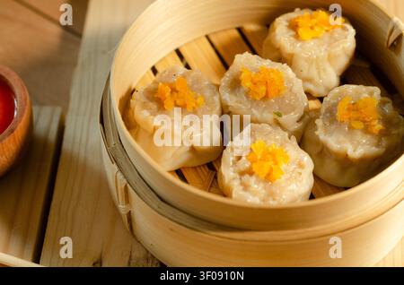 Steamed gyoza dumplings in bamboo steamer with chili sauce on rustic wooden table Stock Photo