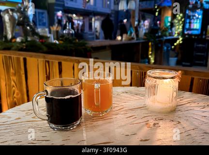 Two glasses of mulled wine punch and a candle on a wooden table in a festive bar setting with blurred people background Stock Photo