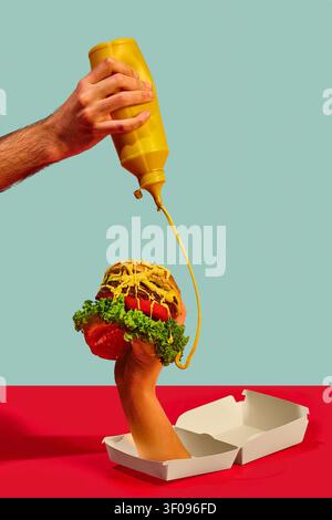 Hands pouring mustard sauce over burger held above white takeaway box on colorful studio background. Stock Photo