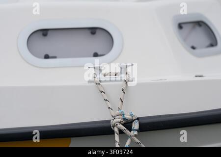 secured boat cleat on calm deck with rope close-up, slightly angled view in marine setting, white and black colors, commercial boating equipment use Stock Photo