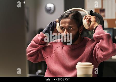 Indian Man Wearing Headphones While Working in Home Office Stock Photo