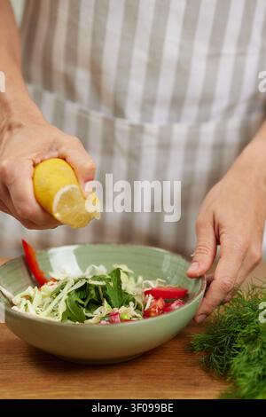 Woman preparing a fresh salad by squeezing lemon juice over a bowl of raw vegetables, promoting healthy eating Stock Photo