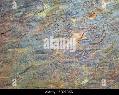 The surface displays a rich stone texture featuring various earthy colors and natural patterns. Light reflects off the rough surface, creating an abst Stock Photo
