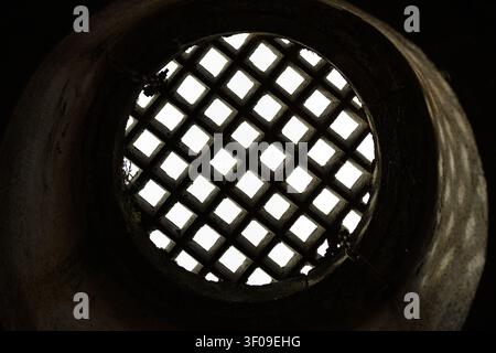 Circular stone opening with iron lattice viewed from below in historic architecture Stock Photo