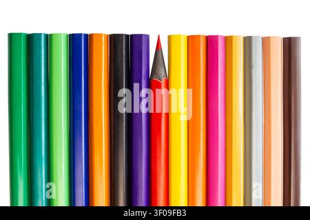 Many colored pencils are lined up in a row with one red pencil positioned differently from the rest. The pencils show different colors. Stock Photo
