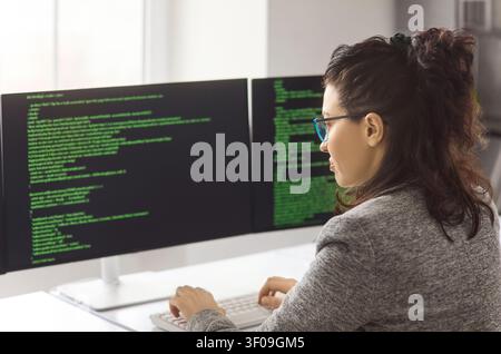 Female programmer coding on dual computer screens in modern office workspace Stock Photo
