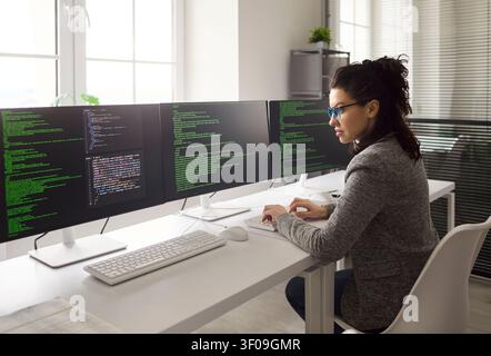 Focused female developer coding software on multi monitor workstation in office Stock Photo