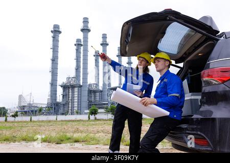 Two professional engineers in safety hard hats consult structural blueprints at an industrial power generation facility. Stock Photo