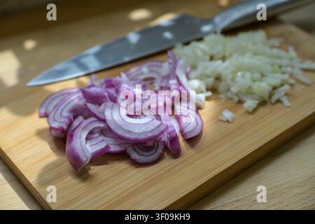 Red and white onions, sliced into half-rings and diced into small cubes on a cutting board with a kitchen knife, preparation for cooking, selected focus, narrow depth of field Stock Photo