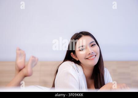 A portrait of a cheerful young woman lying comfortably on a bed in a relaxed home setting representing leisure and wellness. Stock Photo