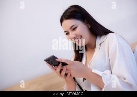 A closeup portrait of a happy young woman using a smartphone while relaxing in a comfortable and bright living space. Stock Photo