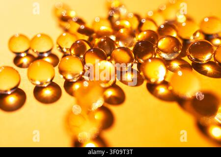 Transparent droplets rest on a golden surface, reflecting light and creating a shimmering effect with soft bokeh in the background Stock Photo