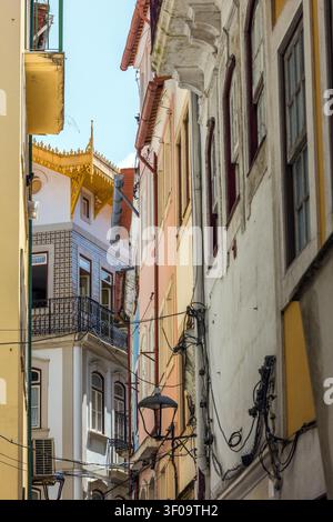 a tight alleyway between historic, multi-colored Portuguese buildings with detailed facades and utility wires against a clear sky. Stock Photo