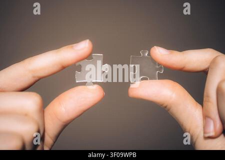 Two hands hold clear plastic puzzle pieces, illustrating the idea of connection and fitting pieces together in a neutral setting Stock Photo