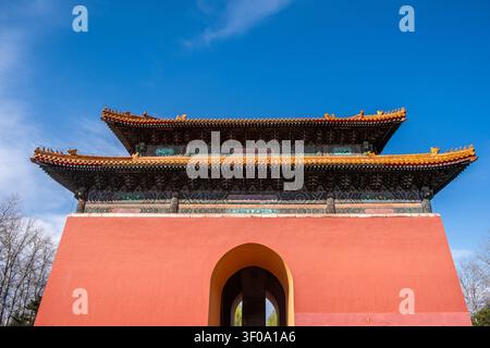 Low-angle view of a red Ming Tombs gate with ornate tiled roof under sunny spring light and blue sky in Beijing, China Stock Photo