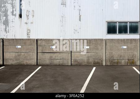Grunge prefab concrete surrounding wall with parking signs. White metallic Industrial building on behind,road in front. Background for copy space Stock Photo