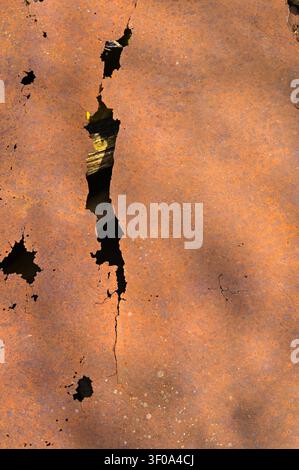 Rusty iron sheet shows distressed vintage background. Corroded metallic surface features huge vertical crack and dark hole. Old metal plate brings ind Stock Photo