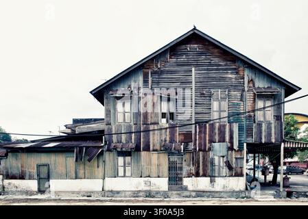 A wide exterior shot of a rustic, two-story traditional building constructed with aged timber planks and rusty corrugated iron sheets under an overcas Stock Photo