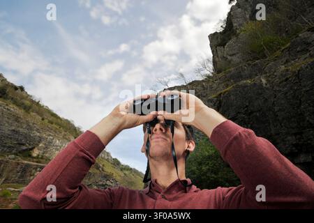 low angle portrait of young man looking at mountain view through binoculars Stock Photo
