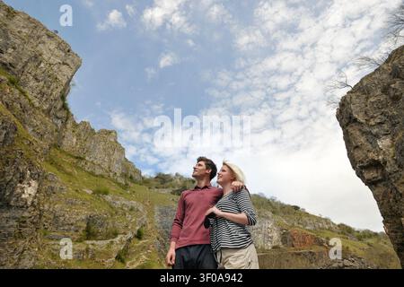 Happy young couple standing hugging and looking at mountain scenery Stock Photo