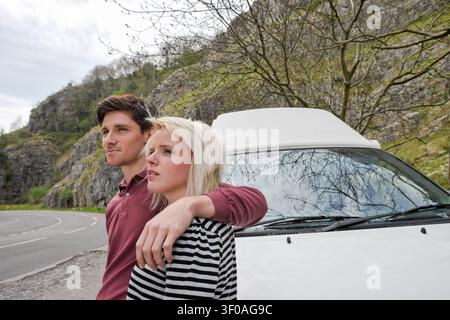 Happy young couple standing in front of motorhome by the side of a road looking at the view Stock Photo